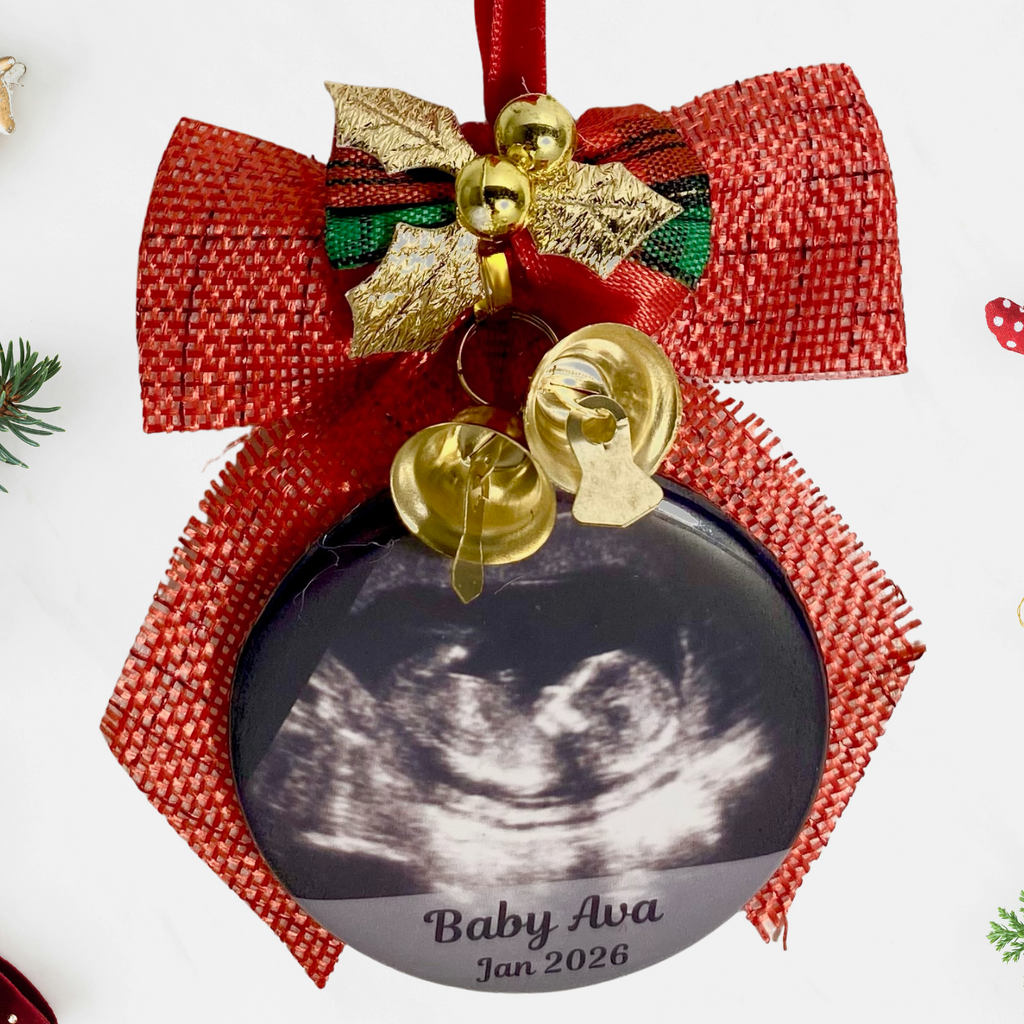 Decorative ornament with ultrasound image and 'Baby Ava' text, surrounded by Christmas decorations on a white background.